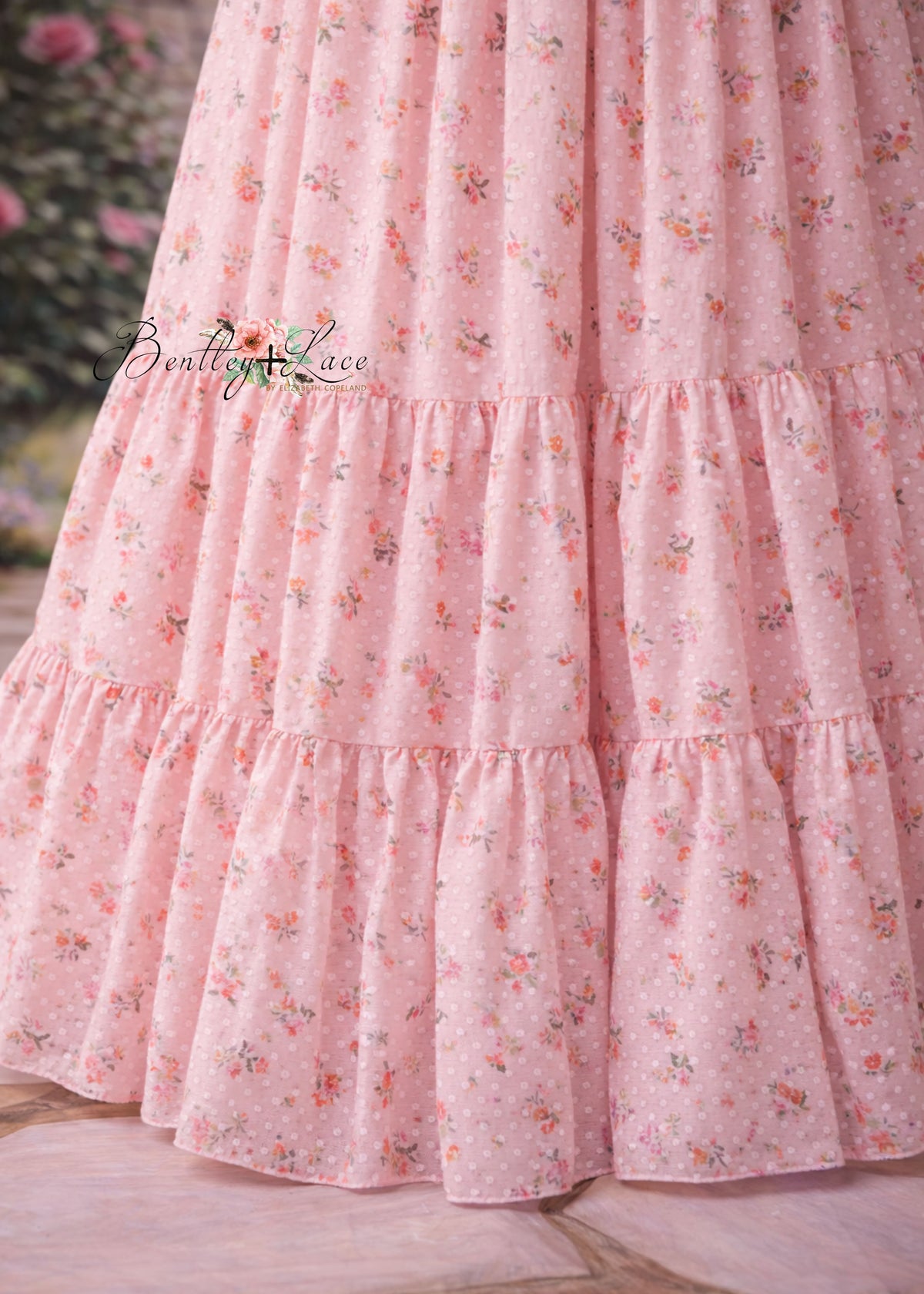 Close-up of a pink floral dress with ruffled layers on a wooden surface.