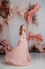Woman in a pink dress standing in front of a decorative backdrop with large bows and flowers.