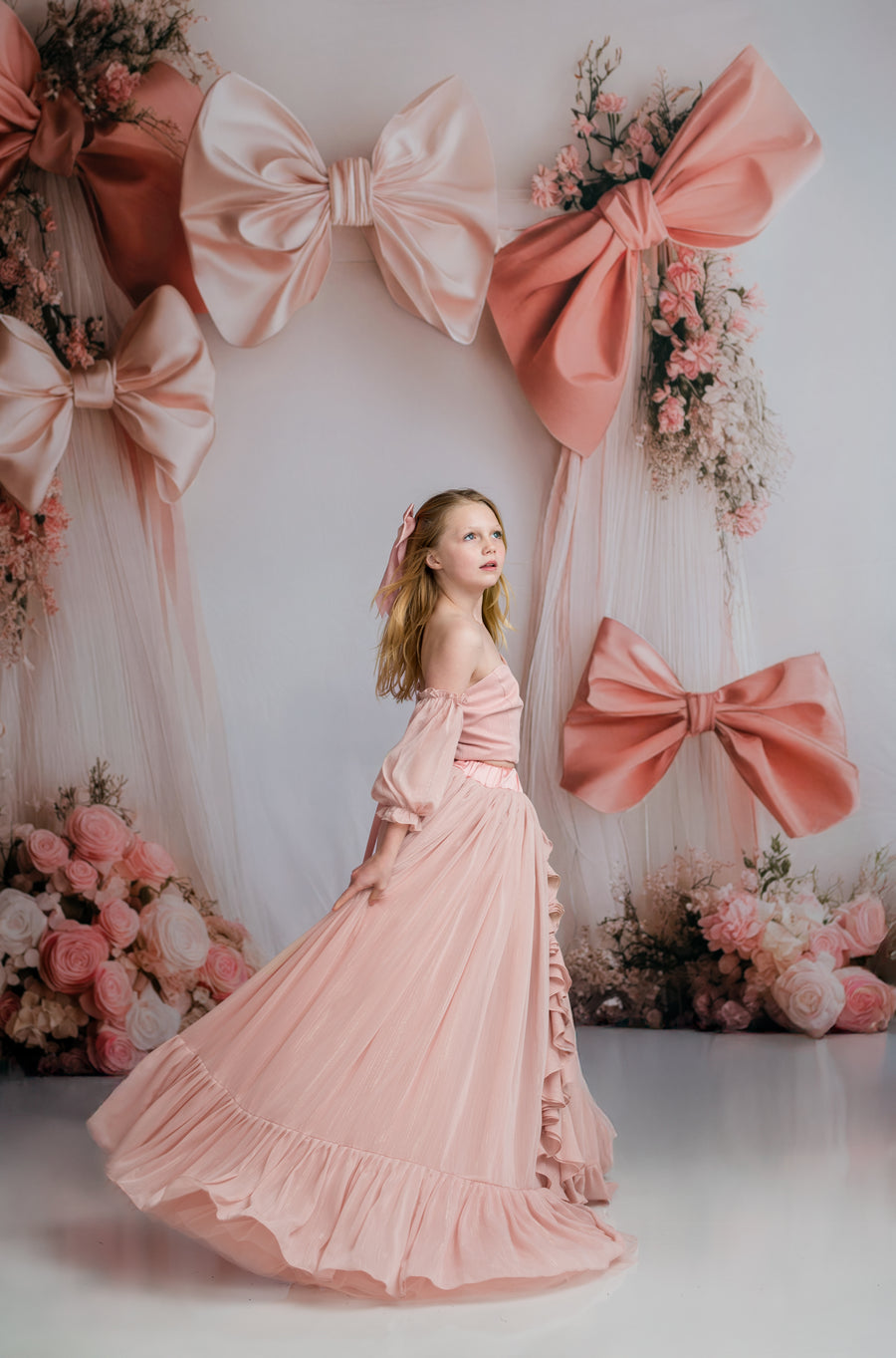 Woman in a pink dress standing in front of a decorative backdrop with large bows and flowers.