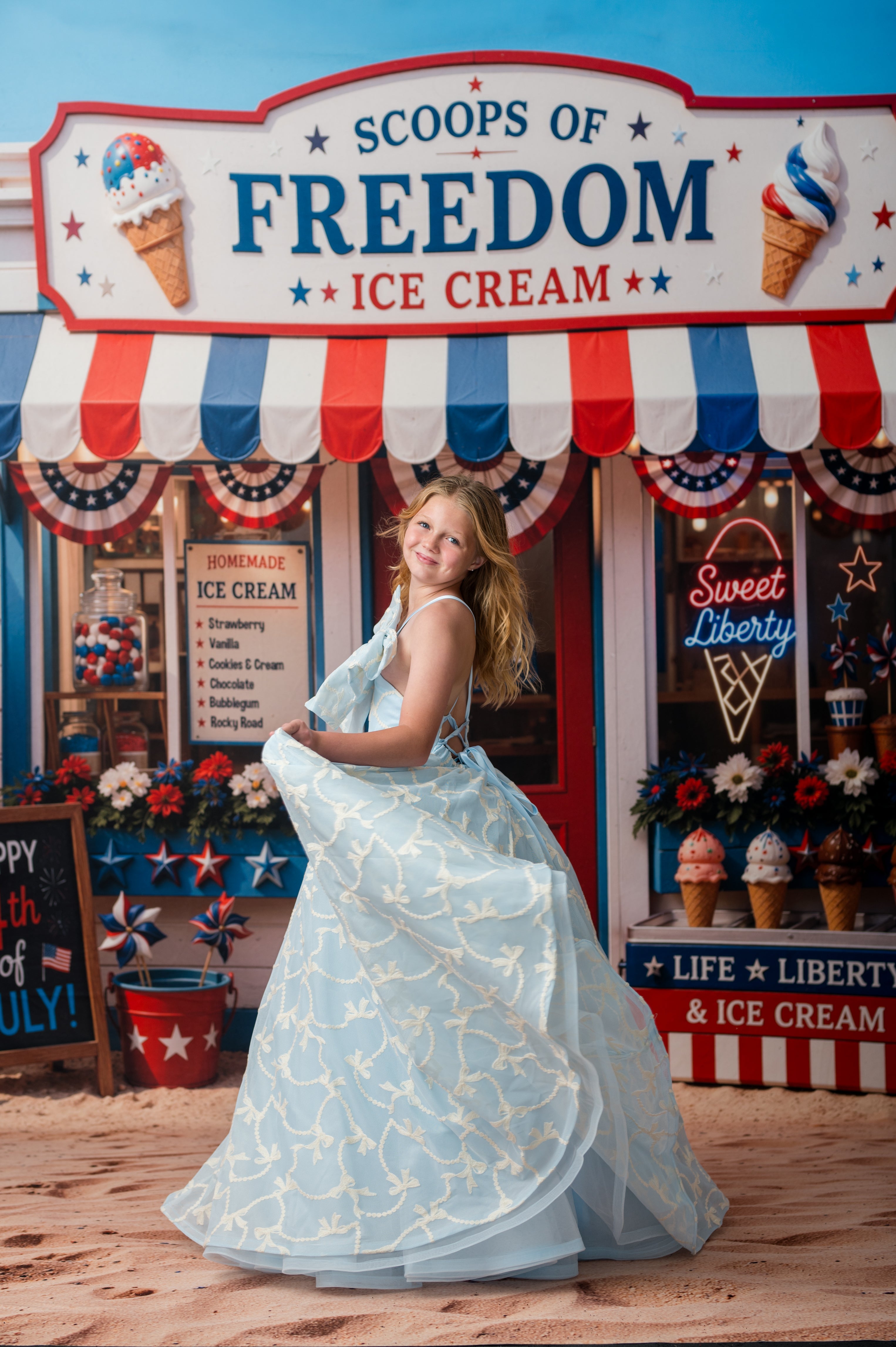 Woman in a light blue dress standing in front of 'Scoops of Freedom Ice Cream' with a patriotic theme.