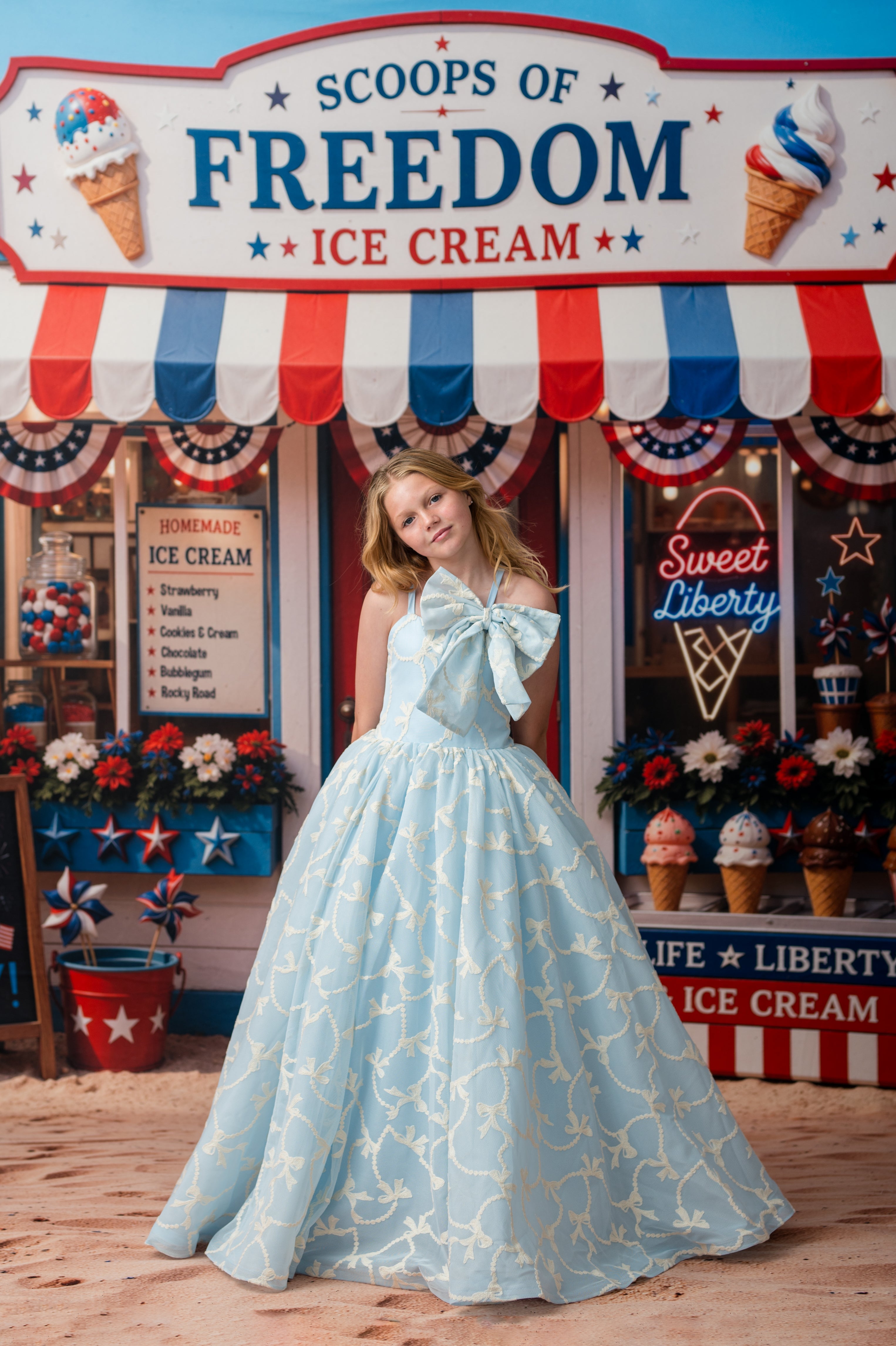 Woman in a blue dress standing in front of 'Scoops of Freedom Ice Cream' with patriotic decor.