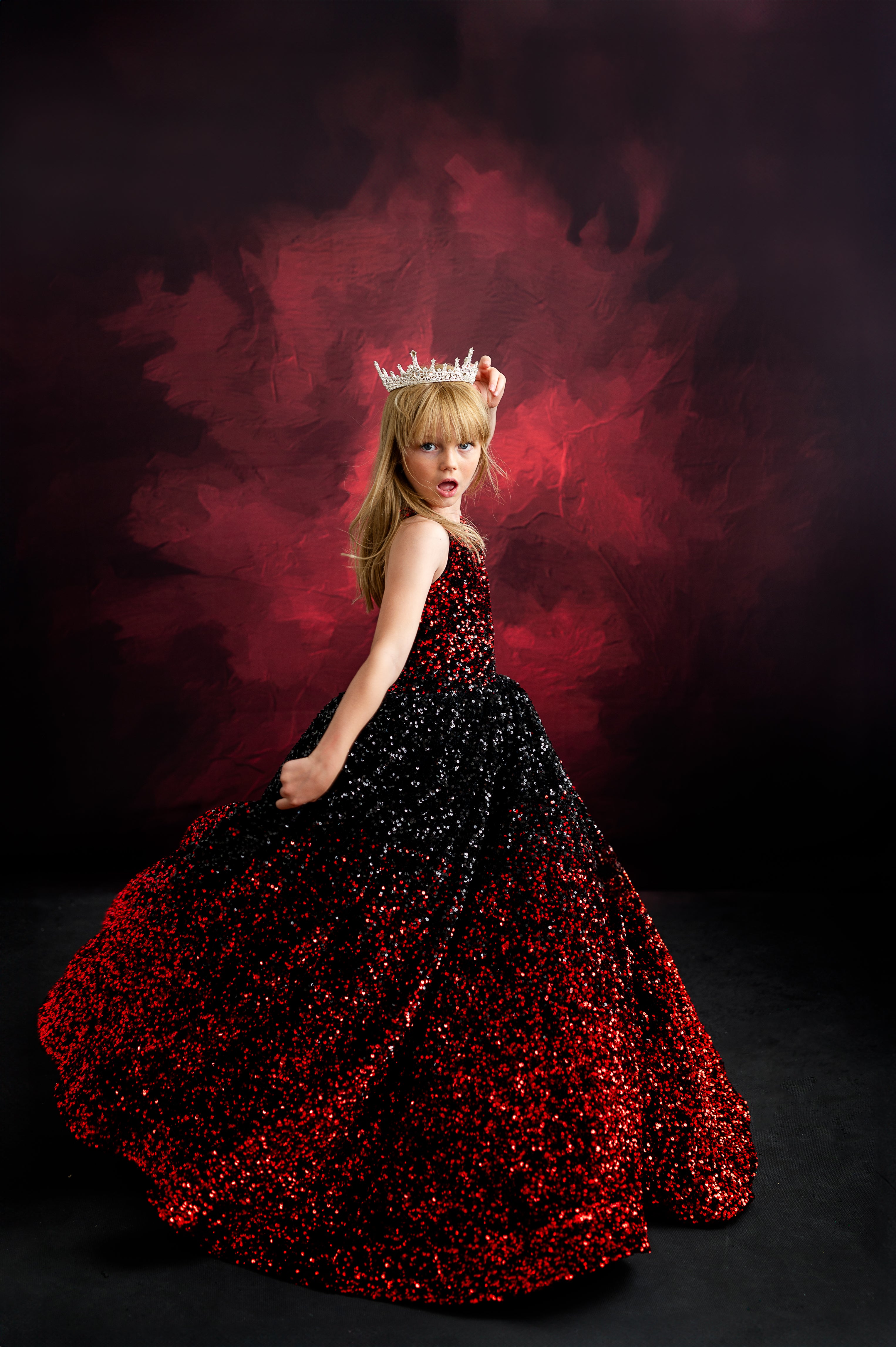 Young girl in a red and black glitter gown channeling Taylor Swift's dramatic "Reputation" era, complete with a crown for a regal look.