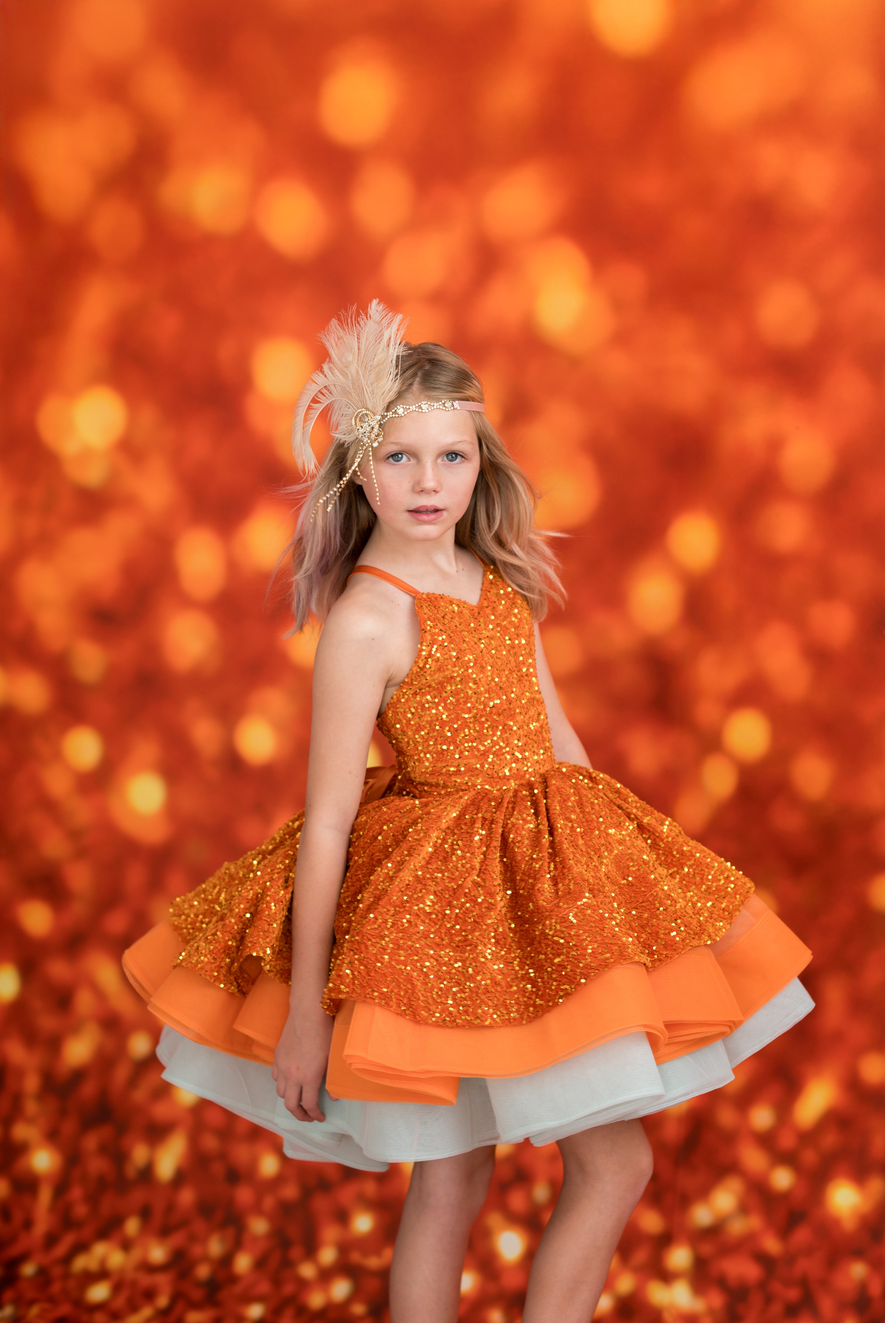 Young girl in an orange dress with a glittery texture against a warm, glowing background.
