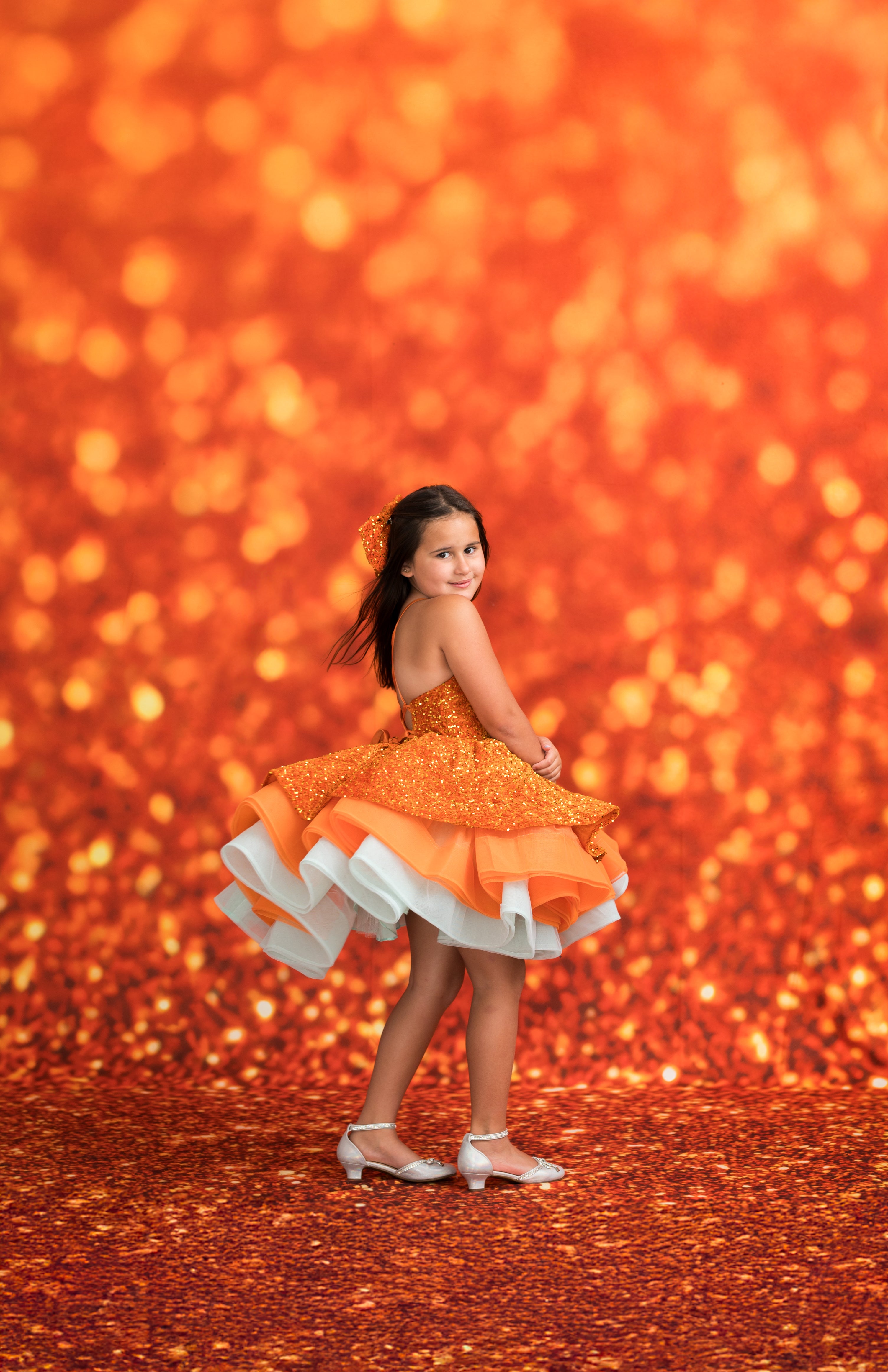 Young girl in an orange dress with white ruffles against a warm, glowing background