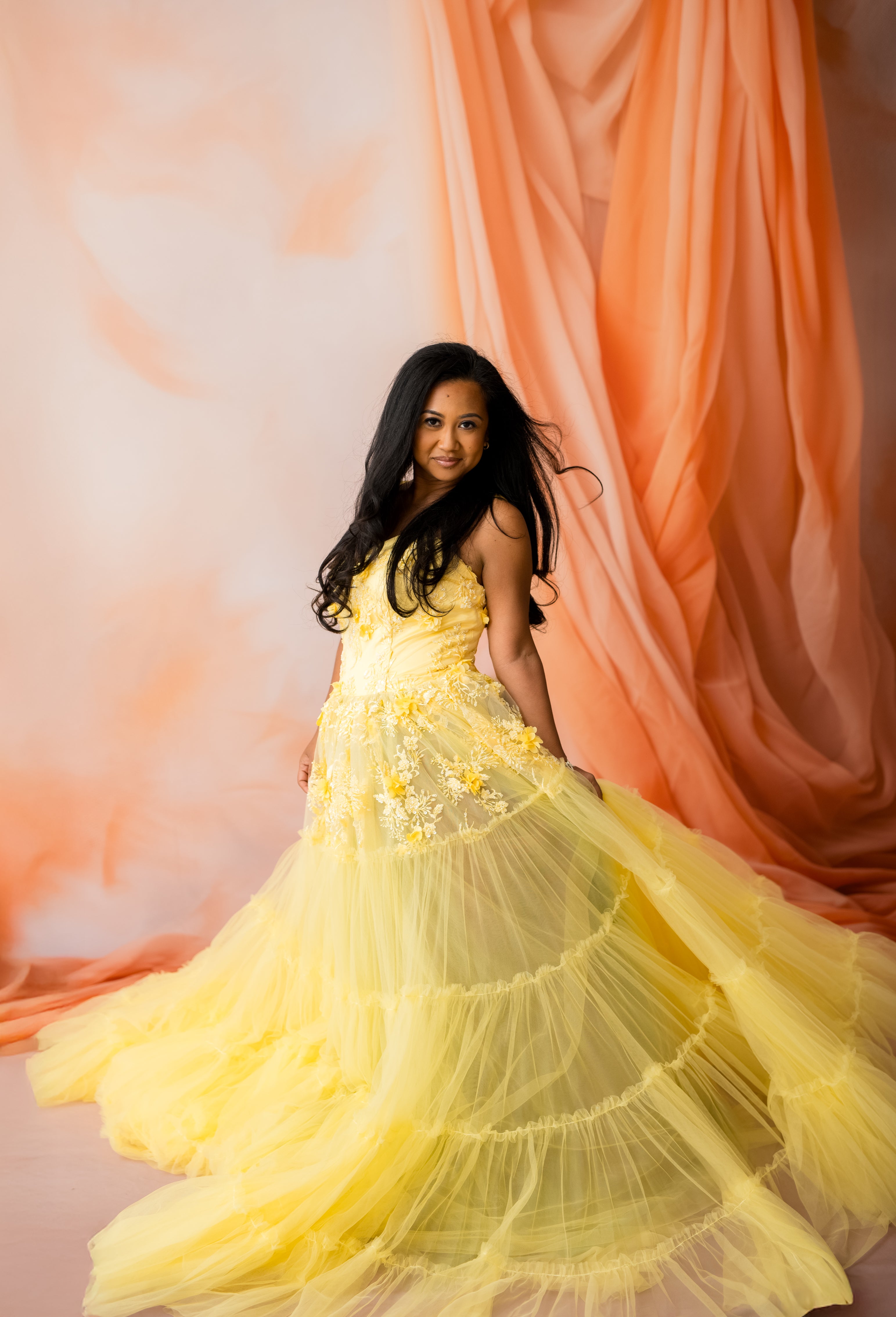 Woman in a yellow dress standing in front of a pink curtain