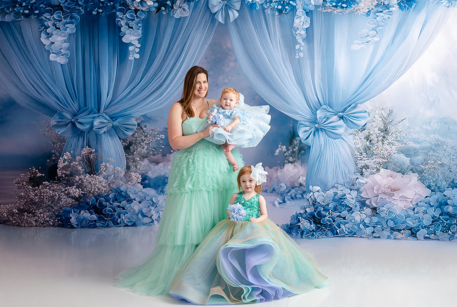 A young girl with a floral hairpiece and a shimmering gold gown looks up at her mother lovingly.
