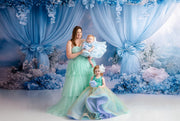 A young girl with a floral hairpiece and a shimmering gold gown looks up at her mother lovingly.
