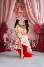 Woman and child in red and white dresses standing in front of floral and bow decorations.