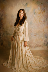 Woman in a flowing beige dress against a textured wall.