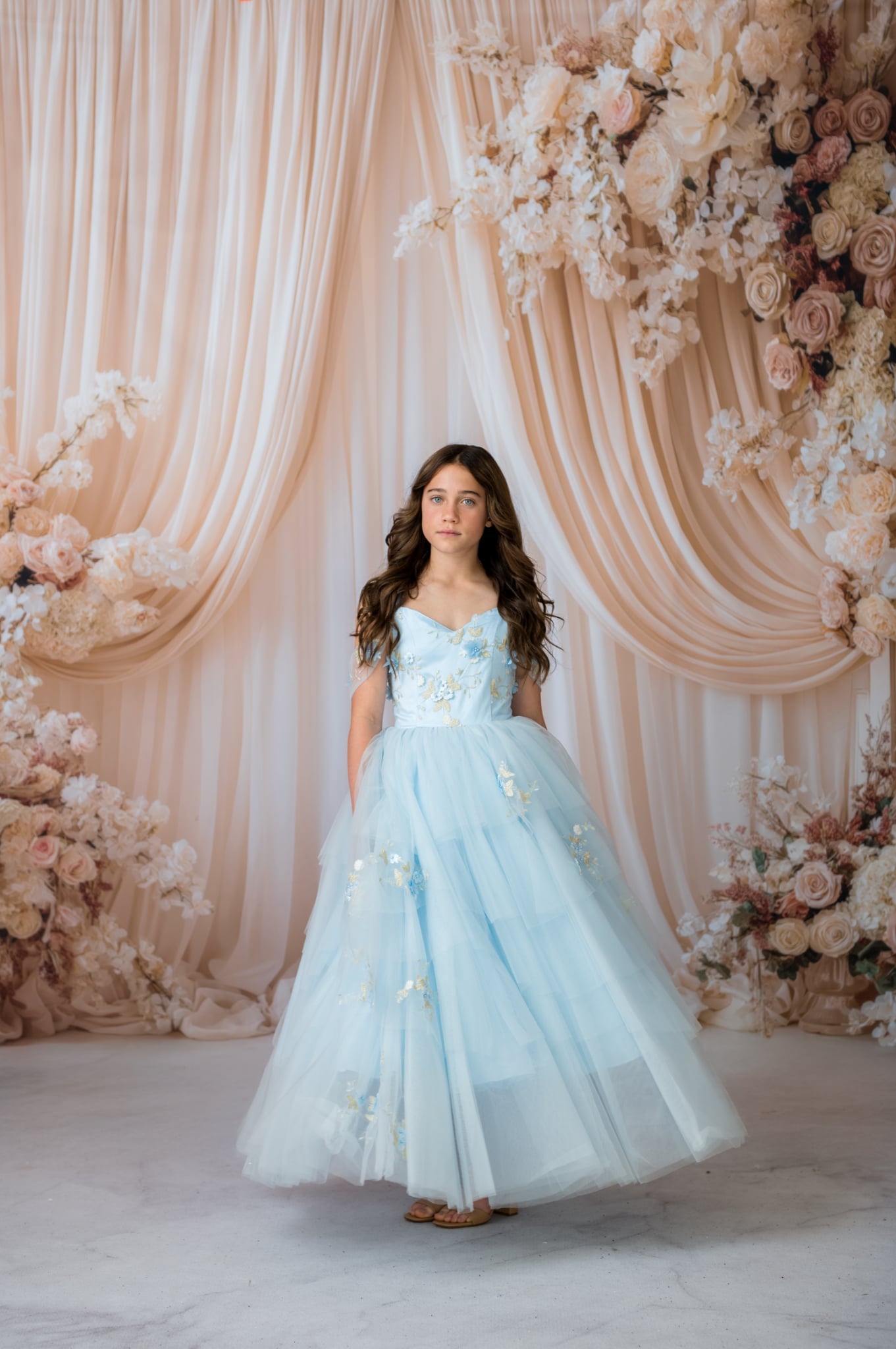 Woman in a light blue dress standing in front of a floral decorated backdrop