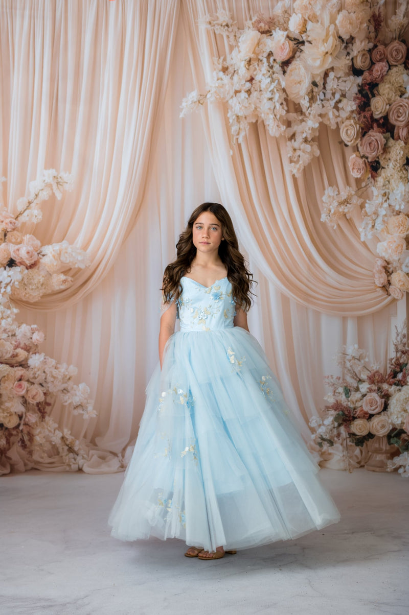 Woman in a light blue dress standing in front of a floral decorated backdrop