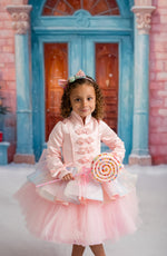 Child wearing a Nutcracker-themed holiday dress with snowy backdrop and Christmas trees.

