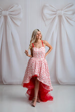 Woman in a red and white floral dress standing against a white background with large bows.