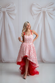 Woman in a red and white floral dress standing against a white background with large bows.