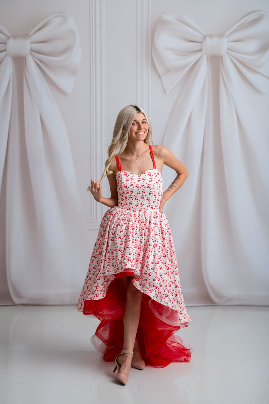 Woman in a red and white floral dress standing against a white background with large bows.