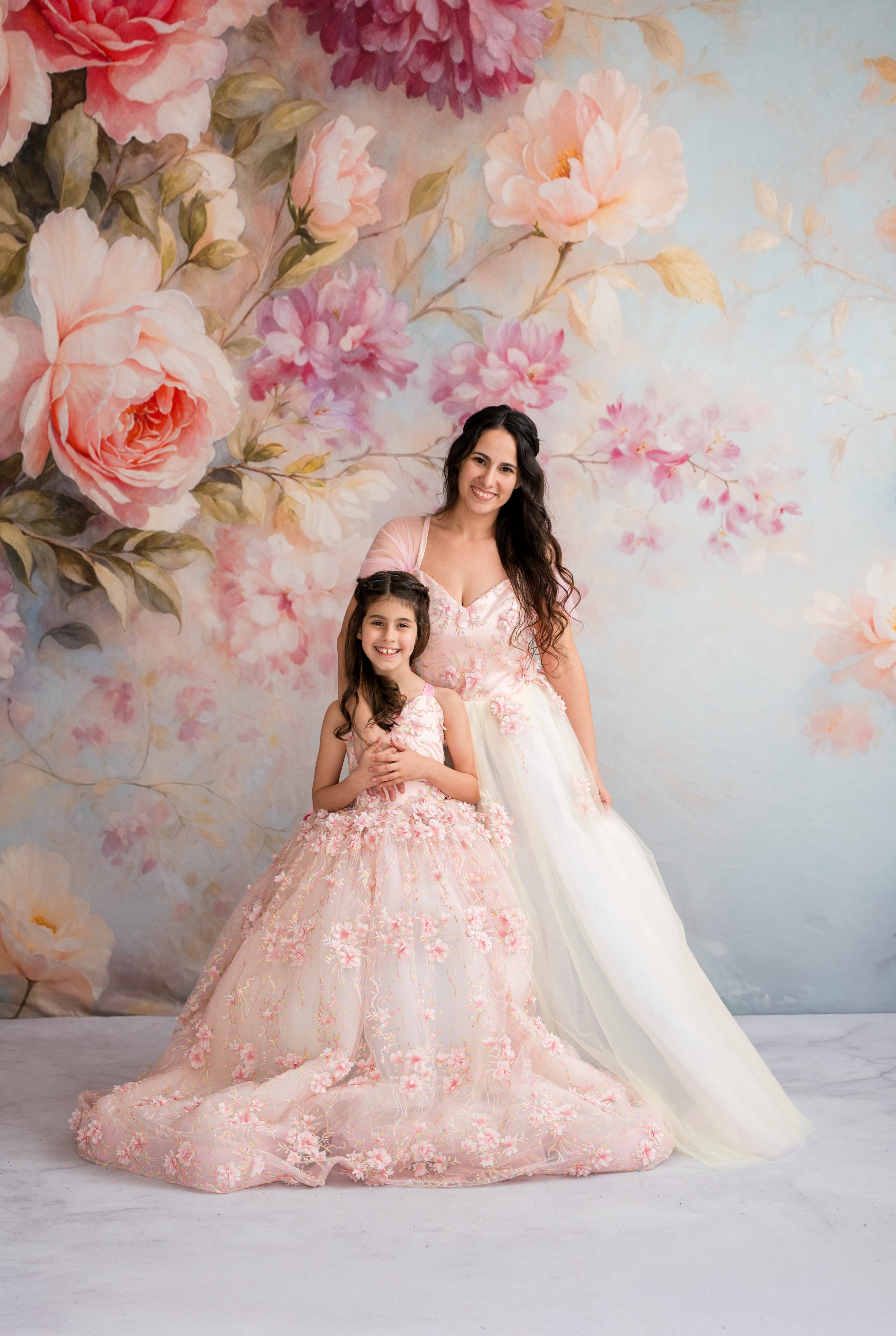 Two women in elegant dresses standing against a floral backdrop