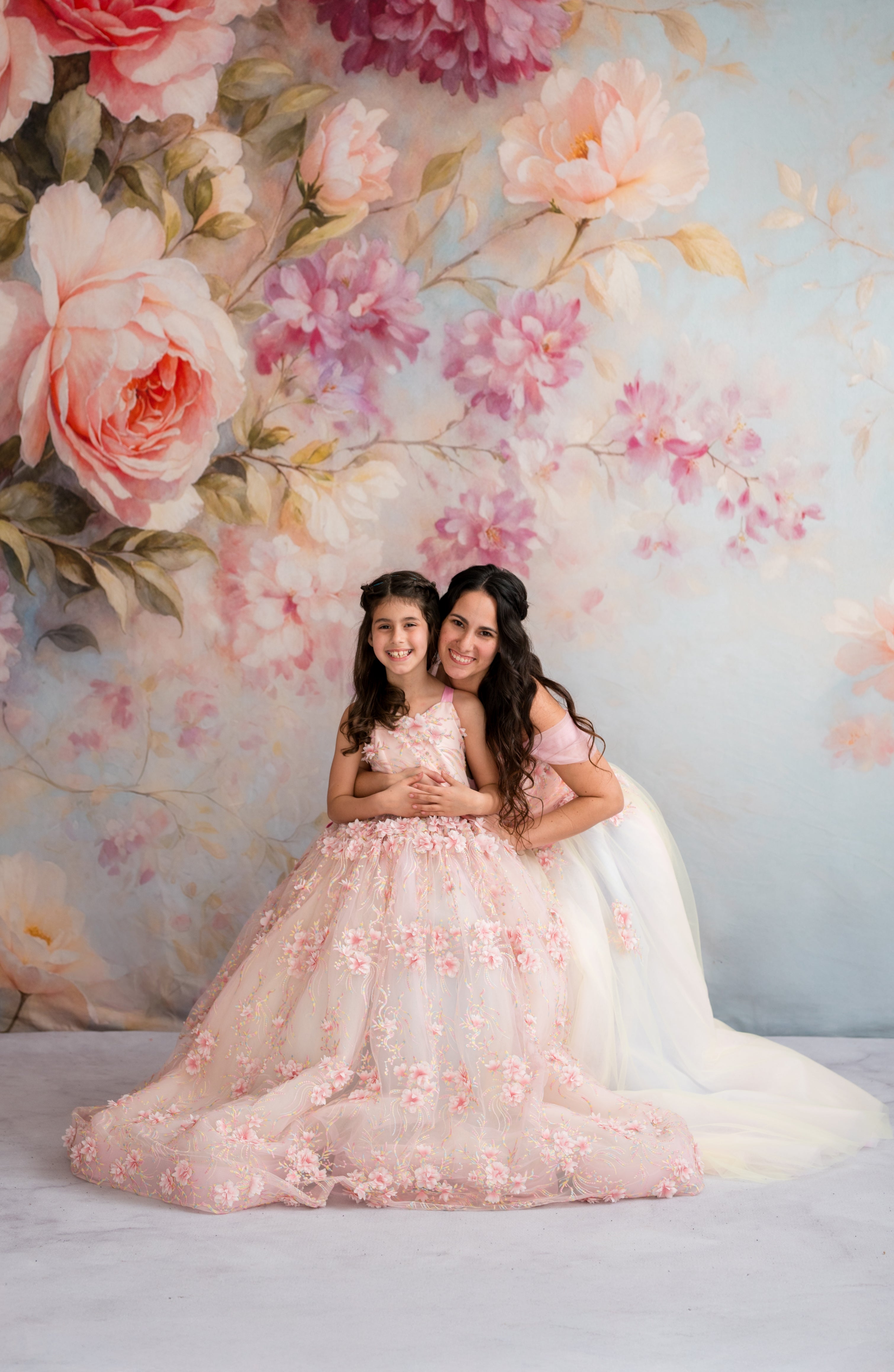 Two women in floral dresses standing in front of a floral backdrop