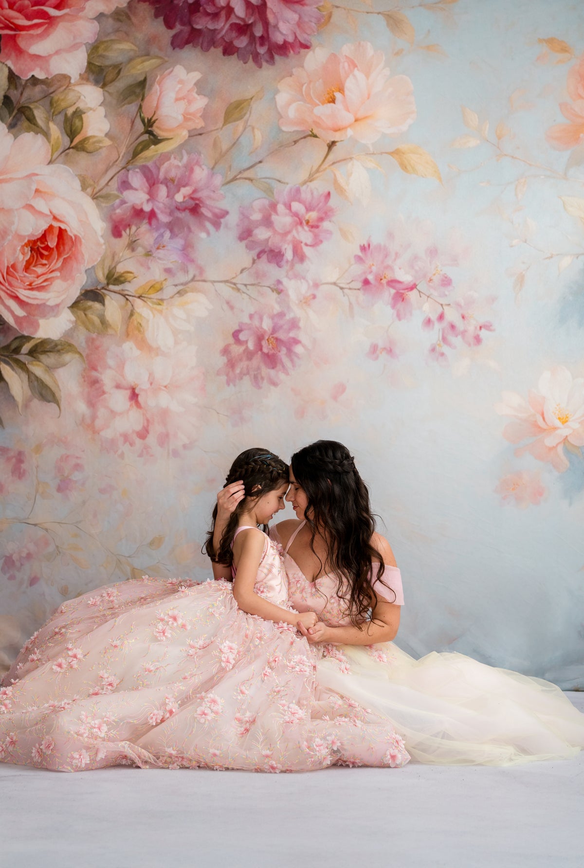 Two women in floral dresses embracing against a floral backdrop