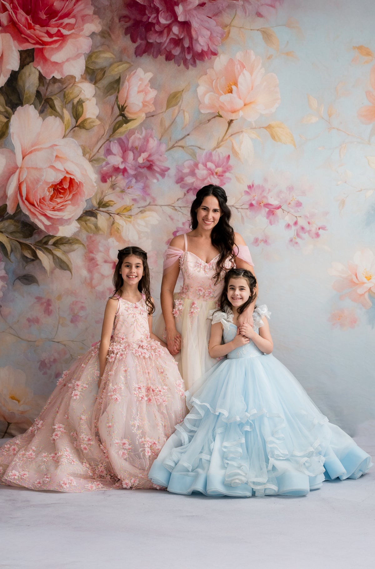 Woman and two young girls in floral dresses standing in front of a floral wall backdrop