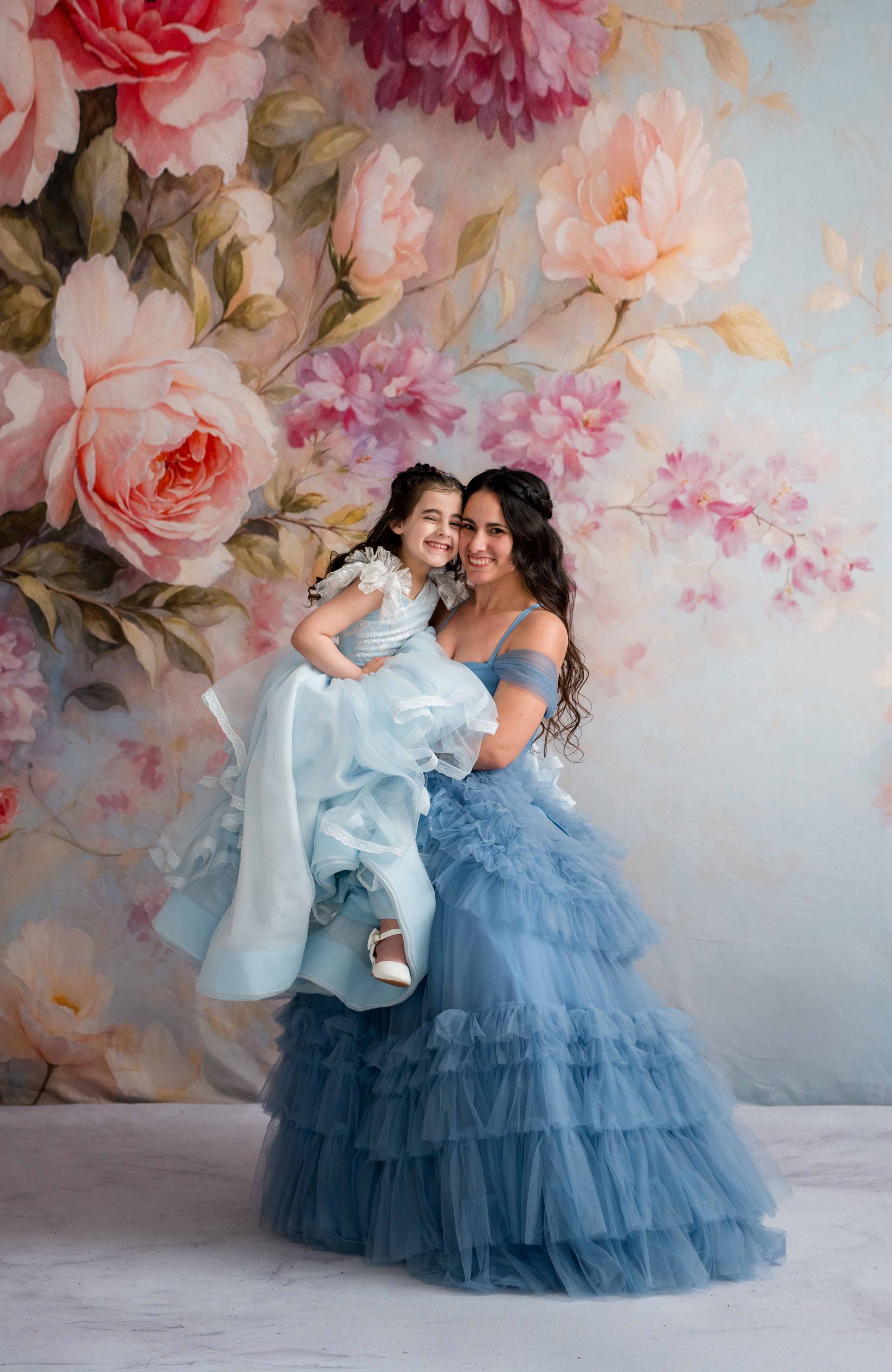 Woman in a blue dress holding a child against a floral backdrop