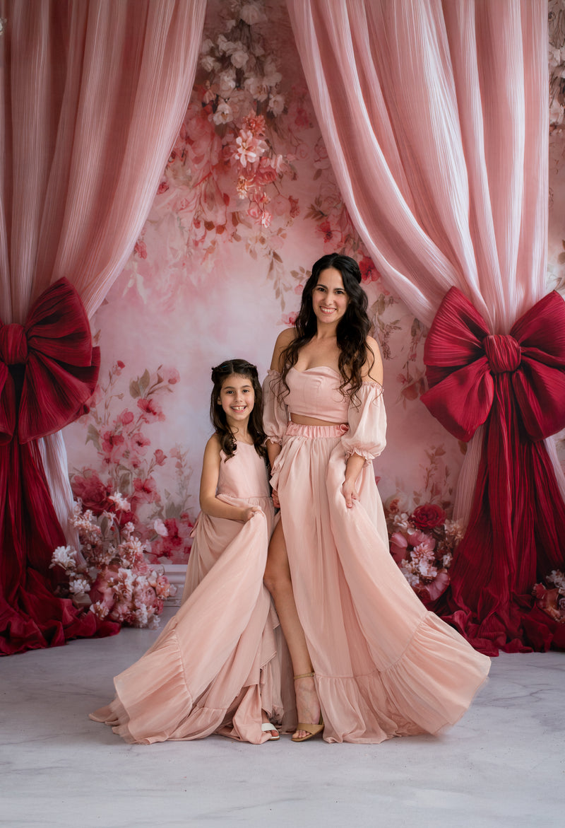 Two women in matching peach dresses standing in front of a decorative floral and curtain backdrop.