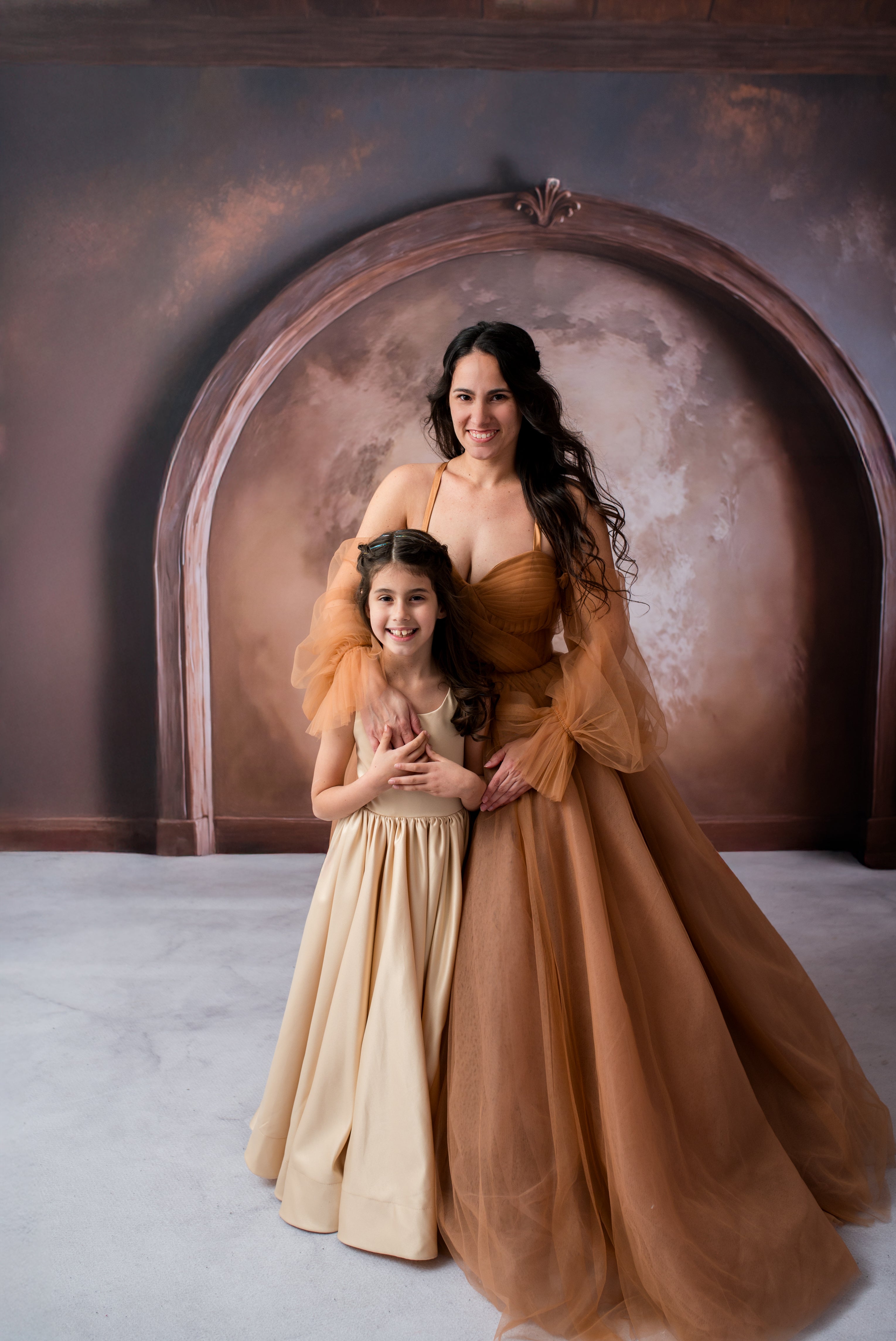 Two women in elegant dresses standing in front of a decorative archway.
