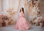 Woman in a pink floral dress standing in front of a floral arch and decorations.