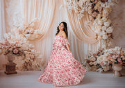 Woman in a pink floral dress standing in front of a floral arch and decorations.