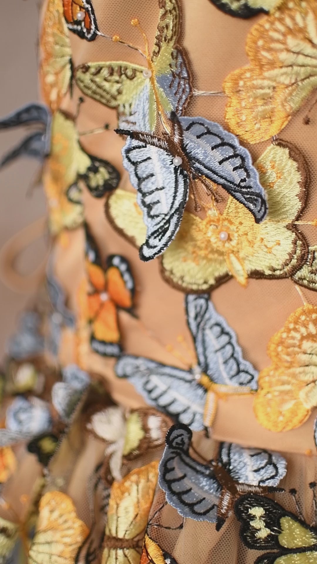 Close-up of a golden dress bodice covered in colorful butterflies, transitioning into a sheer tulle skirt.
