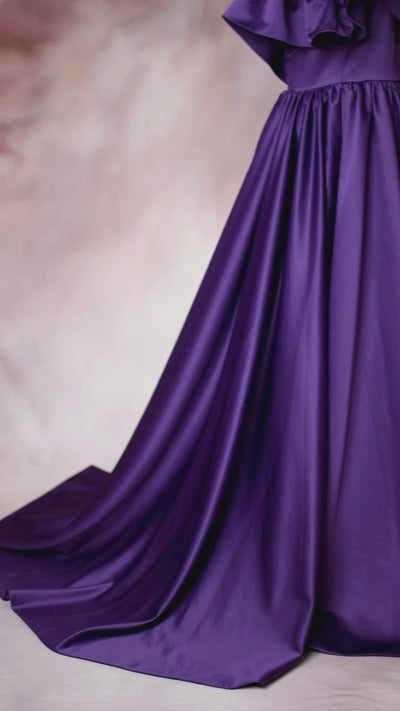 Luxurious purple satin dress with ruffle accents and a long, sweeping train displayed on a mannequin.