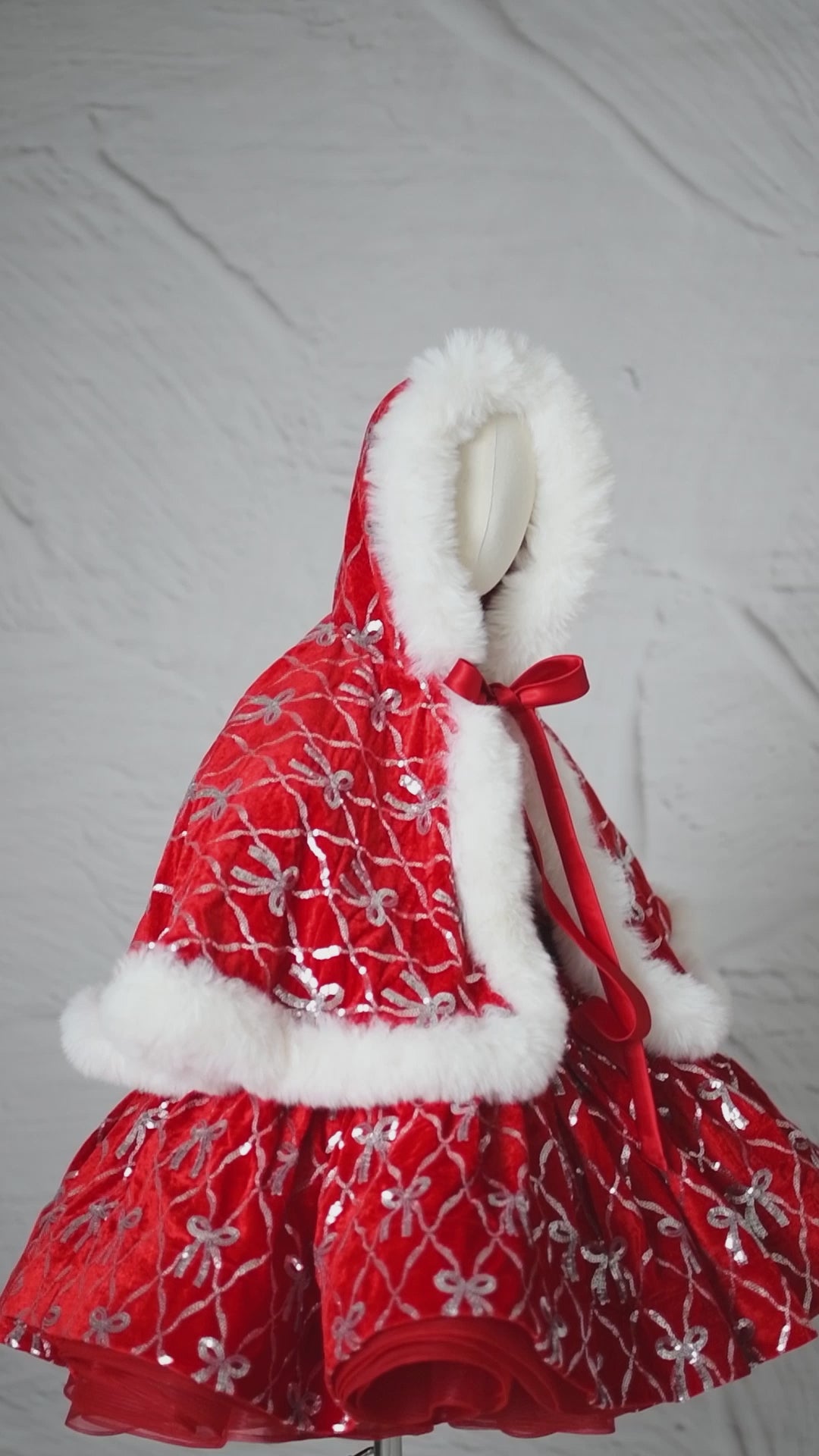 Children’s couture Christmas dress in red velvet with shimmering silver bow design.

