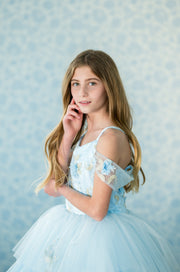 Young girl in a light blue dress with floral details against a patterned blue background