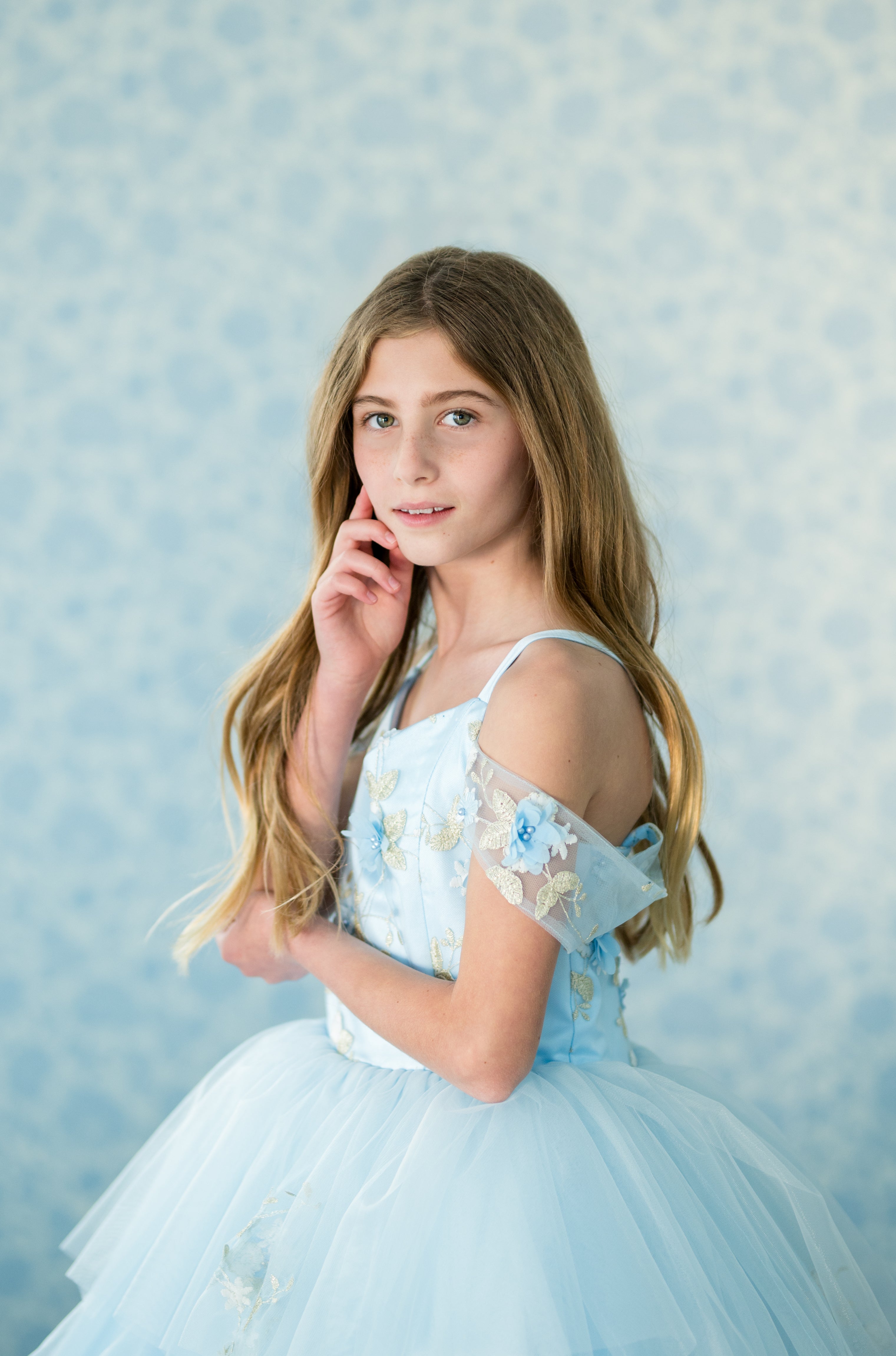 Young girl in a light blue dress with floral details against a patterned blue background