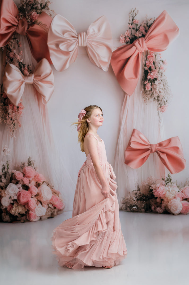 Woman in a pink dress standing in front of a decorative backdrop with large bows and flowers.