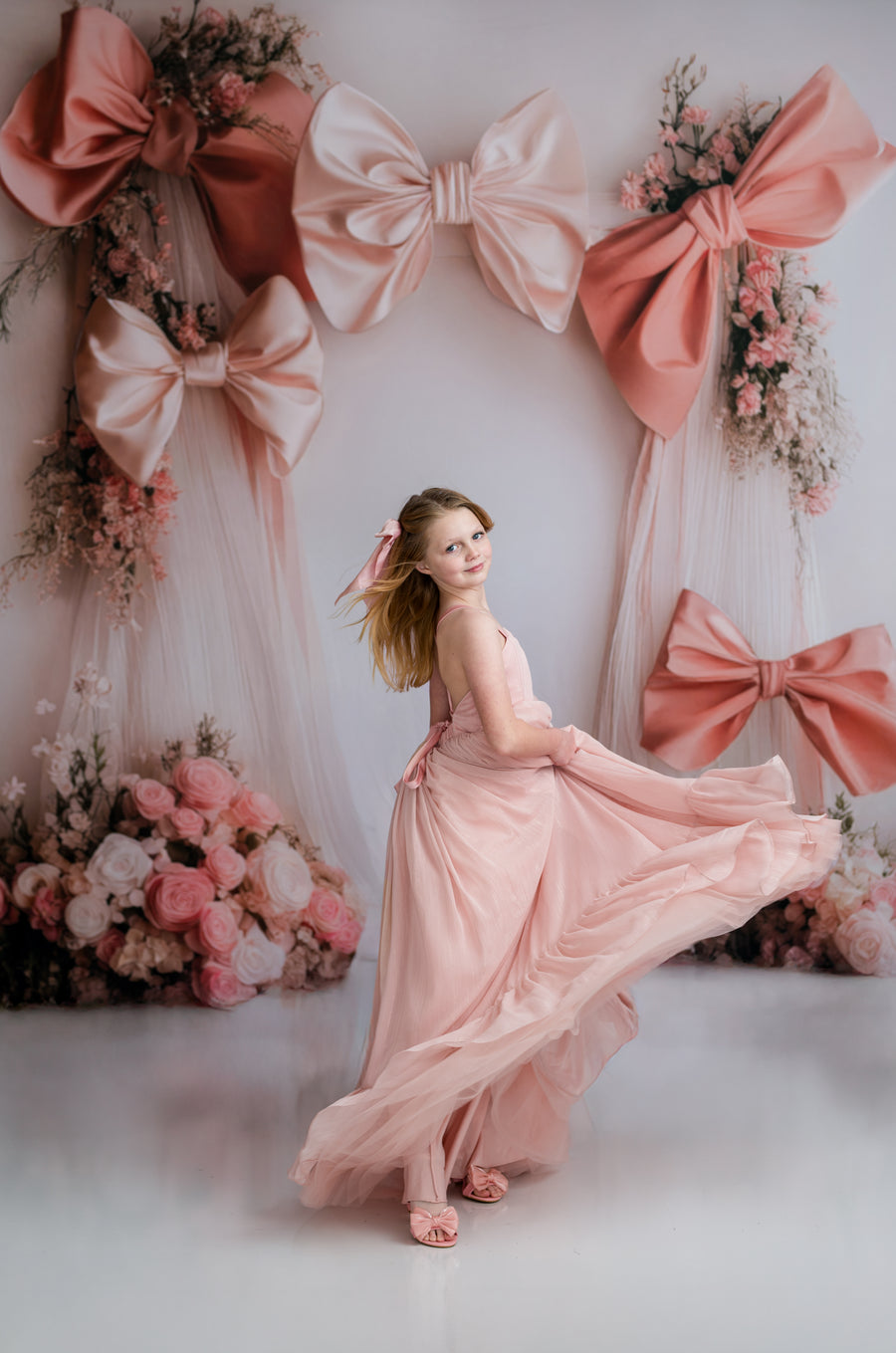 Woman in a pink dress standing in front of a decorative backdrop with large bows and flowers.