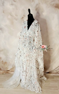 A white gown with 3D butterfly tulle embellishments, displayed on a mannequin with a floral silk fabric background.