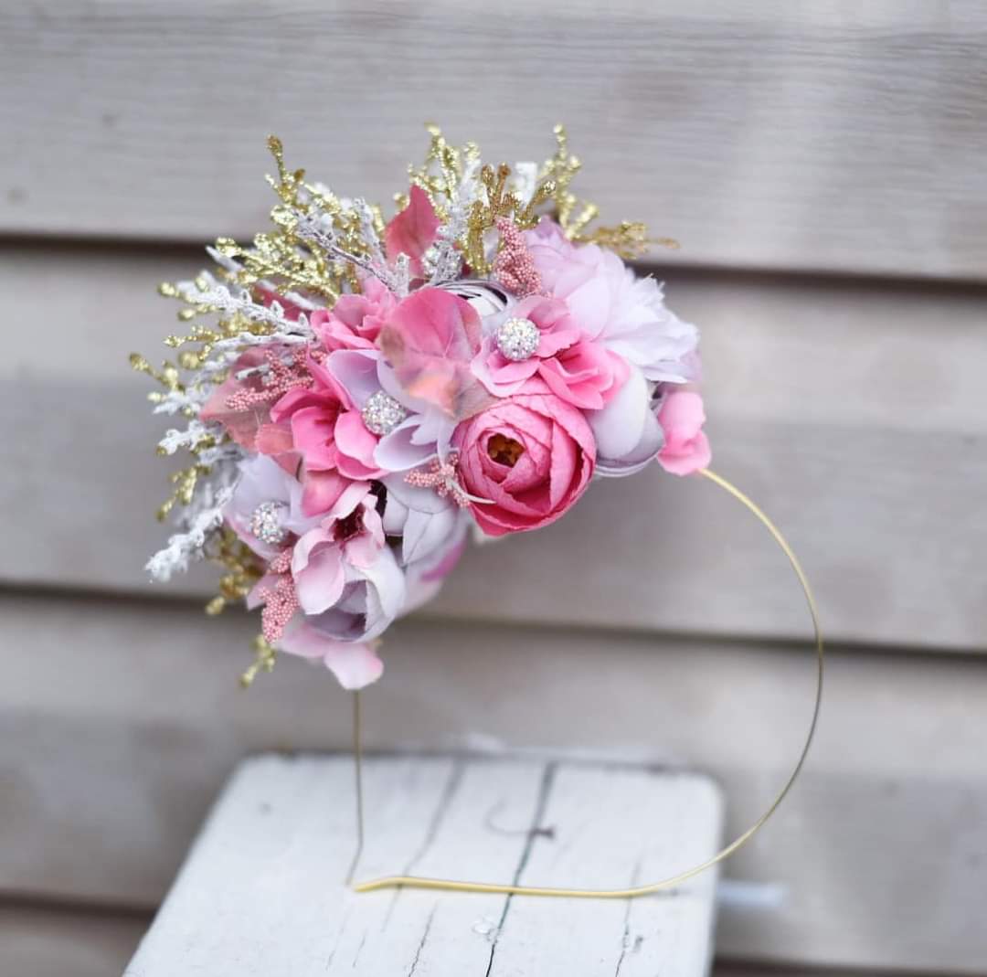 A pink and gold floral headband displayed on a wooden surface.